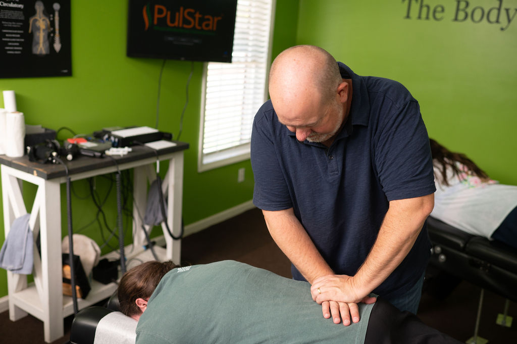 Dr. Mike Geran performing a manual chiropractic adjustment on a patient's lower back in the treatment room at Foothills Chiropractic in Travelers Rest, SC