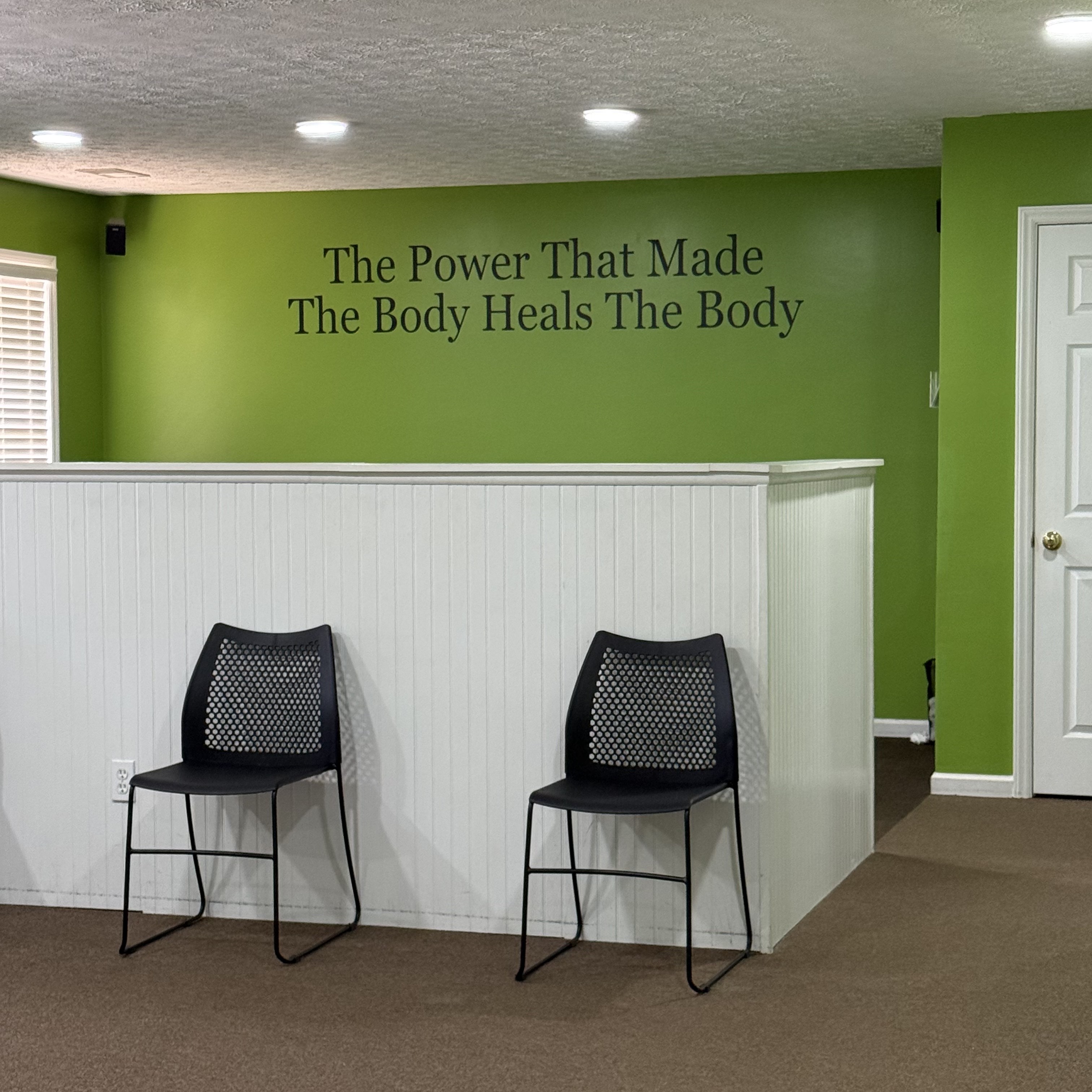 Foothills Chiropractic waiting area in Travelers Rest, SC — green walls, black chairs, and the motto 'The Power That Made The Body Heals The Body'